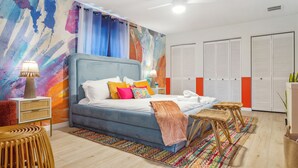 A modern bedroom with a large bed, colorful artwork, and a ceiling fan. - Pickleball, Basketball, Heated Pool, Mini Golf! (Seminole)