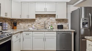 A modern kitchen with white cabinets, a brick backsplash, stainless steel appliances, and a granite countertop. - Pickleball, Basketball, Heated Pool, Mini Golf! (Seminole)