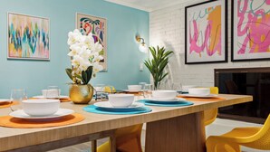 A dining area with a long table set for four, surrounded by vibrant artwork, a vase of white orchids, and yellow chairs. - Pickleball, Basketball, Heated Pool, Mini Golf! (Seminole)