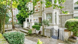 Un immeuble à plusieurs étages, doté d’une façade blanche, d’une enseigne portant le numéro « 53 », et d’un petit jardin avec un banc et un arbre.