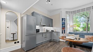Une cuisine moderne avec des meubles gris, un grand réfrigérateur et un coin repas comprenant une table ronde et un canapé bleu.