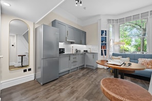 A modern kitchen with grey cabinets, a large refrigerator, and a dining area with a round table and blue sofa.
