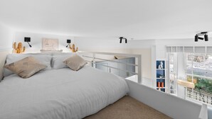Une chambre avec un grand lit, une fenêtre donnant sur un beau paysage, un ventilateur de plafond et une étagère intégrée où sont exposés des objets décoratifs.