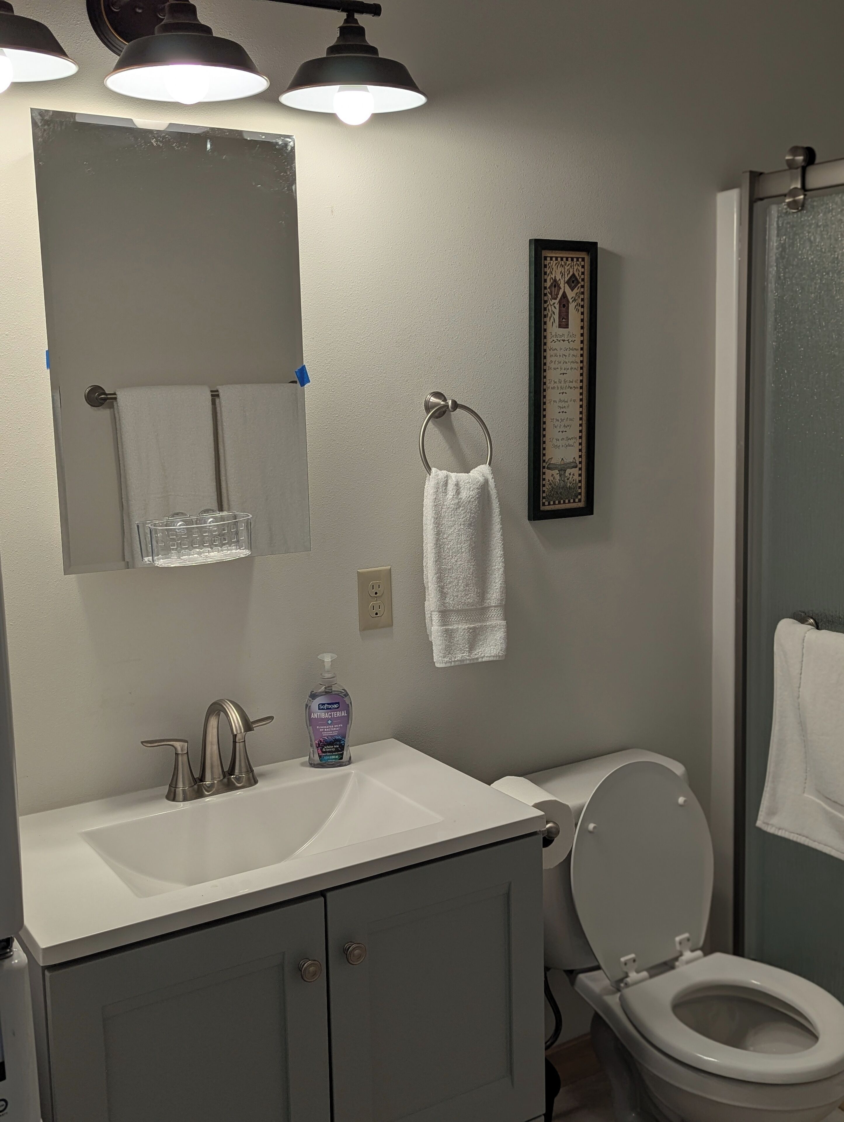 Ein Badezimmer mit einem weißen Waschbecken, einer Toilette, einem Spiegel und einem gerahmten Bild an der Wand.