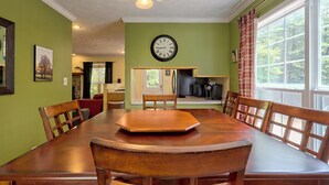 Een eetruimte met een houten tafel en stoelen, een klok aan de muur en een raam met gordijnen.