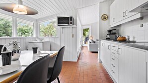 A modern kitchen with white cabinetry, a dining area with a table and chairs, and a view of the outdoors through large windows. - Beach front home in Nykøbing Sj with WiFi (Nykøbing Sj)