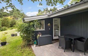 A dark-colored building with a small patio area featuring a table and chairs, surrounded by potted plants and a grassy area. - Beach front home in Nykøbing Sj with WiFi (Nykøbing Sj)