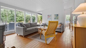 A modern living room with a grey sofa, a yellow armchair, and a dining table. There are large windows offering a view of greenery outside. - Beach front home in Nykøbing Sj with WiFi (Nykøbing Sj)