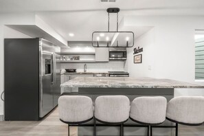 Une cuisine moderne dotée d’un réfrigérateur en acier inoxydable, d’un îlot en marbre avec des tabourets de bar et d’un luminaire suspendu.