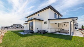 Une maison moderne à deux étages, dotée d’un patio couvert, d’une pelouse bien entretenue et d’un système de climatisation.