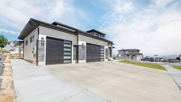 Une maison moderne à deux étages, dotée d’un garage, d’une allée et surplombant un ciel dégagé.