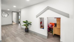Une pièce spacieuse avec un plancher en bois, une plante en pot et un espace de jeu équipé de jouets et d’une poussette rose.