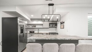 Une cuisine moderne dotée d’un réfrigérateur en acier inoxydable, d’un îlot en marbre avec des tabourets de bar et d’un luminaire suspendu.