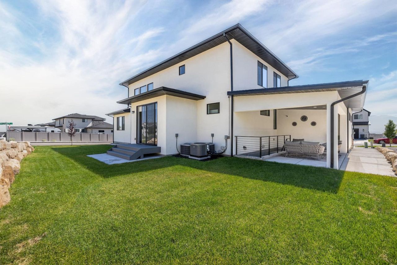 Una casa moderna de dos pisos con un patio cubierto, un césped bien cuidado y una unidad de aire acondicionado.