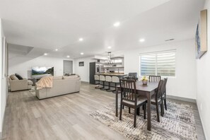 Un salon moderne comprenant un canapé, une table à manger avec des chaises et un coin cuisine avec des tabourets de bar.