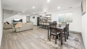 Un salon moderne comprenant un canapé, une table à manger avec des chaises et un coin cuisine avec des tabourets de bar.
