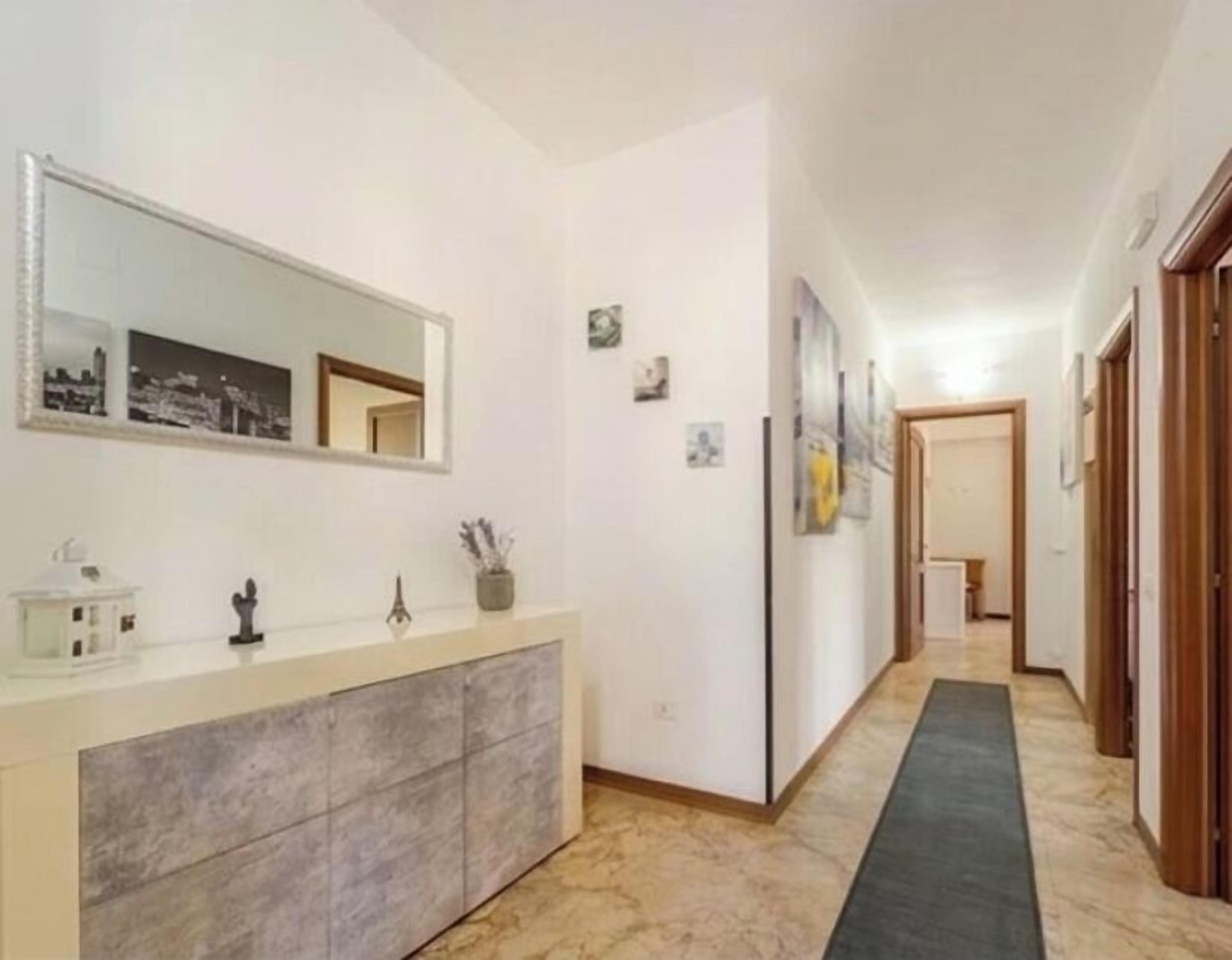 A hallway with a marble floor, a white console table with a mirror, and a door at the end.