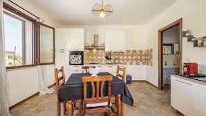 A compact kitchen with white cabinets, a dining table with chairs, a hanging light fixture, and a view through a window.