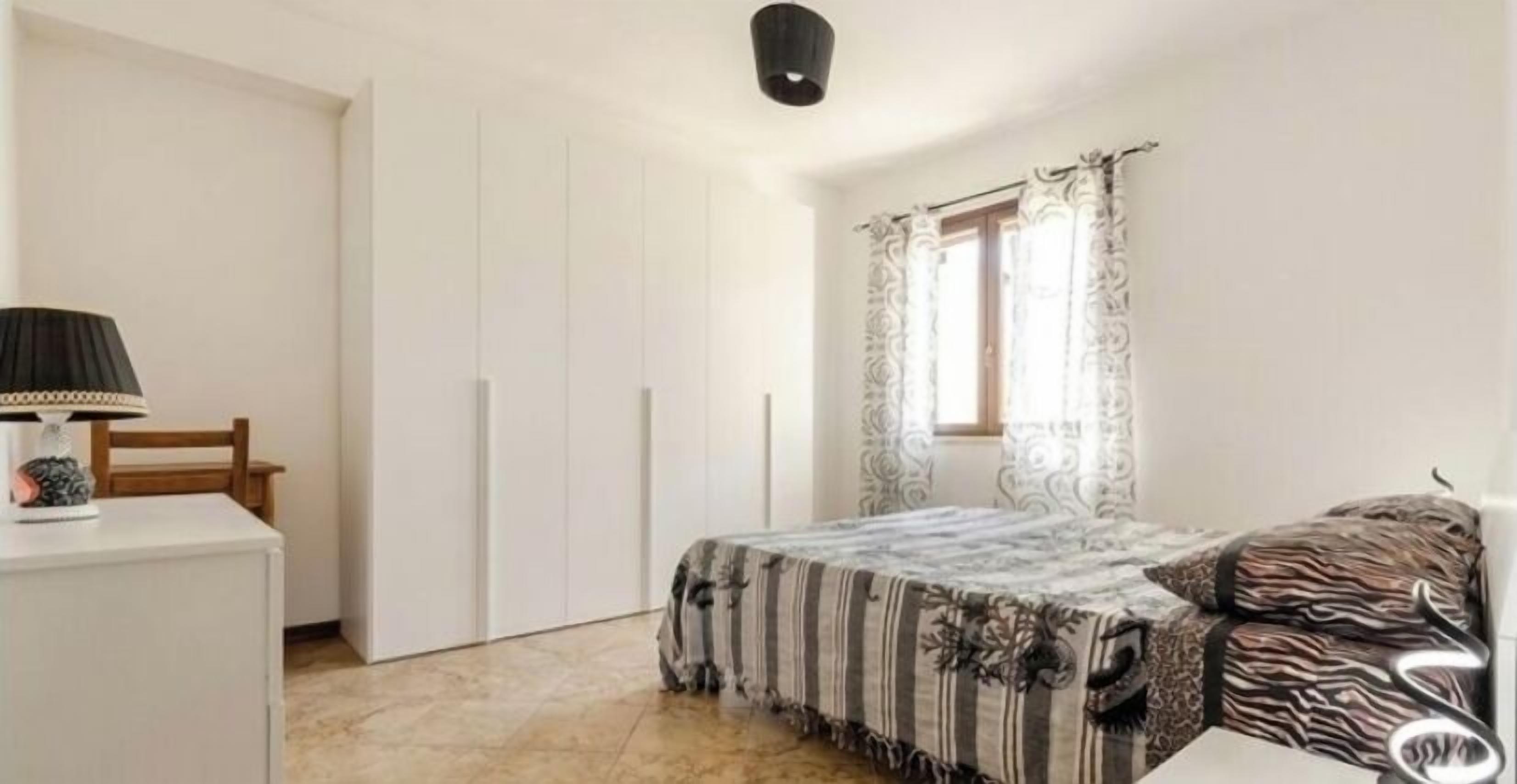 Une chambre à coucher avec un lit, un bureau, une chaise, une armoire et une fenêtre avec des rideaux.
