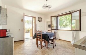 A dining area with a table and chairs, a clock on the wall, and a window with a view of greenery.