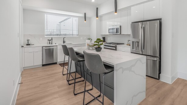 A modern kitchen with white cabinetry, a stainless steel refrigerator, and a marble island with bar stools.
