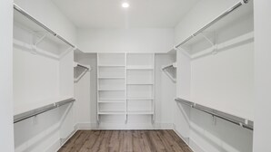 A walk-in closet with wooden flooring, white walls, and metal shelving units.