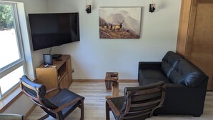 Ett vardagsrum med en platt-TV, en tavla, ett träskåp och två läderfåtöljer.