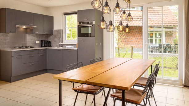 A modern kitchen with grey cabinets, a wooden dining table, and a large window with a view of a brick building. - Holiday Home in Bad Bentheim Near Dutch Border (Bad Bentheim)