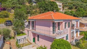 Eine rosa Villa mit rotem Ziegeldach, einem Balkon und einer Treppe, die zum Eingang führt.