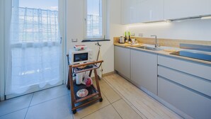 Een moderne keuken met witte kasten, een roestvrijstalen spoelbak en een houten aanrecht. Er staat een kleine kar met een magnetron en waterkoker.