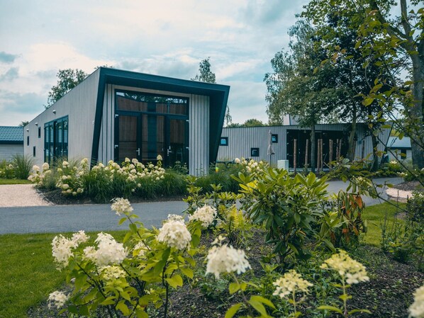 Ein modernes Gebäude mit großen Glasfenstern und einer Metallfassade, umgeben von einem gepflegten Garten mit verschiedenen Pflanzen und Blumen.