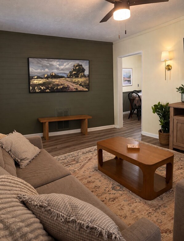 A living room with a sofa, a coffee table, a painting, and a ceiling fan.