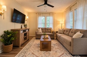 A living room with a sofa, a coffee table, a TV, and a ceiling fan. - Pet-Friendly Downtown Cottage: Dogs Stay FREE- Near Wedding Venues (Bremen)