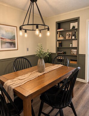 A dining area with a wooden table, black chairs, a vase with flowers, and a pendant light.