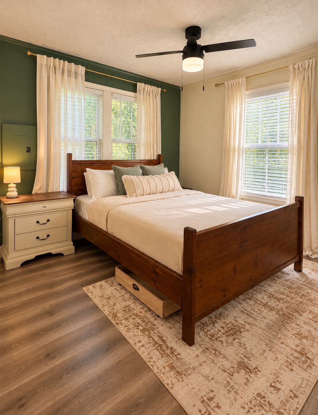 A bedroom with a wooden bed, a nightstand, a ceiling fan, and a window with curtains.