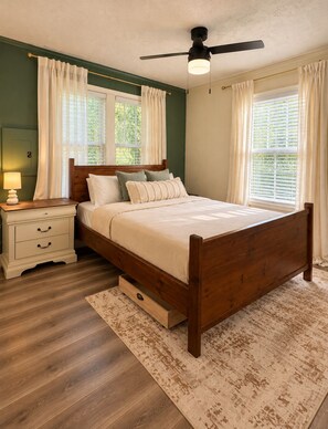 A bedroom with a wooden bed, a nightstand, a ceiling fan, and a window with curtains. - Pet-Friendly Downtown Cottage: Dogs Stay FREE- Near Wedding Venues (Bremen)