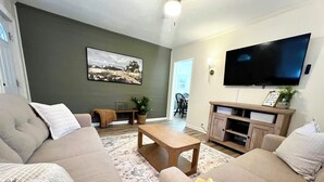 Una sala de estar con sofá, mesa de centro y televisor de pantalla plana montado en la pared.