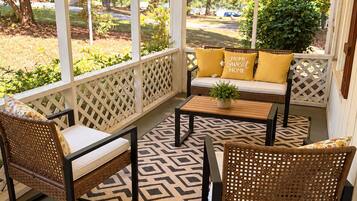 A covered porch with wicker furniture, a patterned rug, and a view of the outdoors.