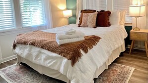 A bedroom with a bed, two bedside lamps, a nightstand, and a window with blinds. - Pet-Friendly Downtown Cottage: Dogs Stay FREE- Near Wedding Venues (Bremen)