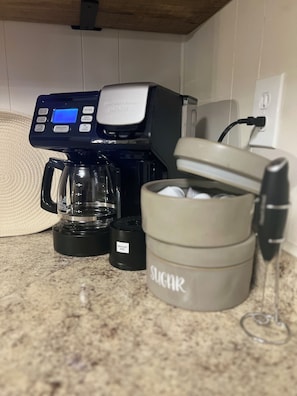 Una cafetera, un recipient de vidre, un recipient de sucre i una paret blanca amb una presa elèctrica.