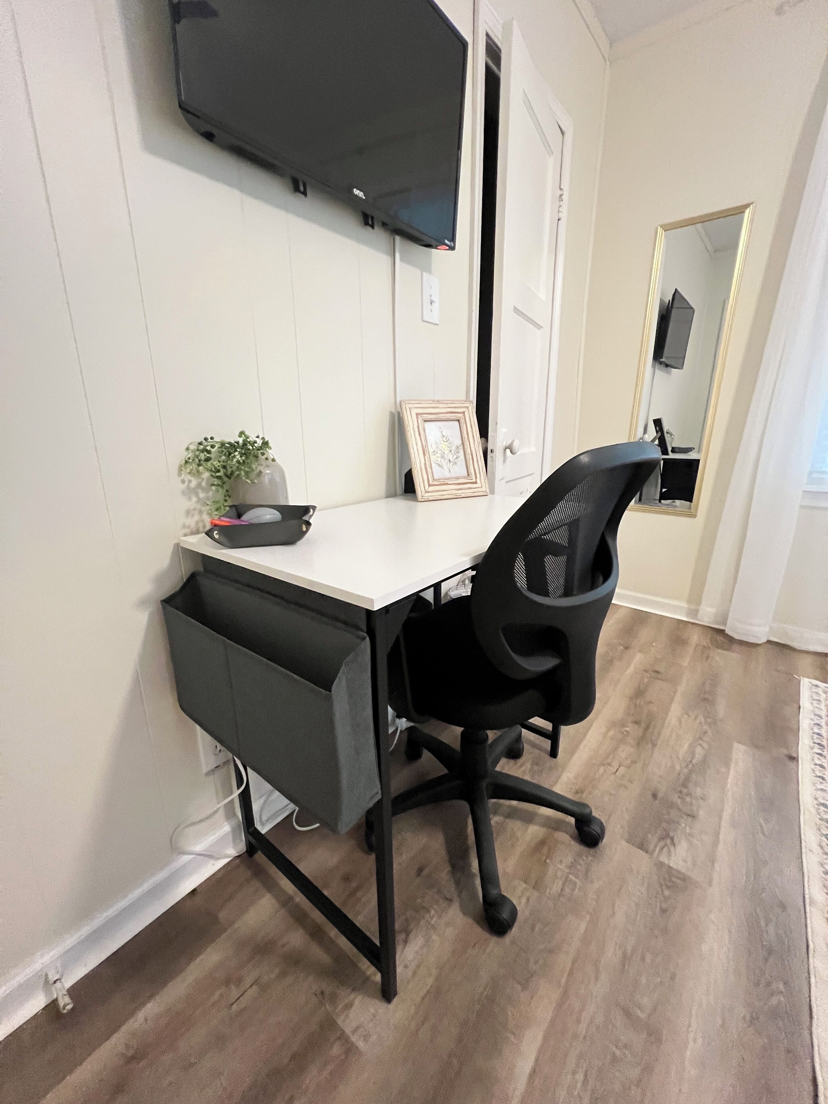 Un espace de bureau moderne avec un bureau blanc, un fauteuil de bureau noir et un téléviseur à écran plat fixé au mur.