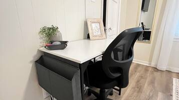 Un espace de bureau moderne avec un bureau blanc, un fauteuil de bureau noir et un téléviseur à écran plat fixé au mur.