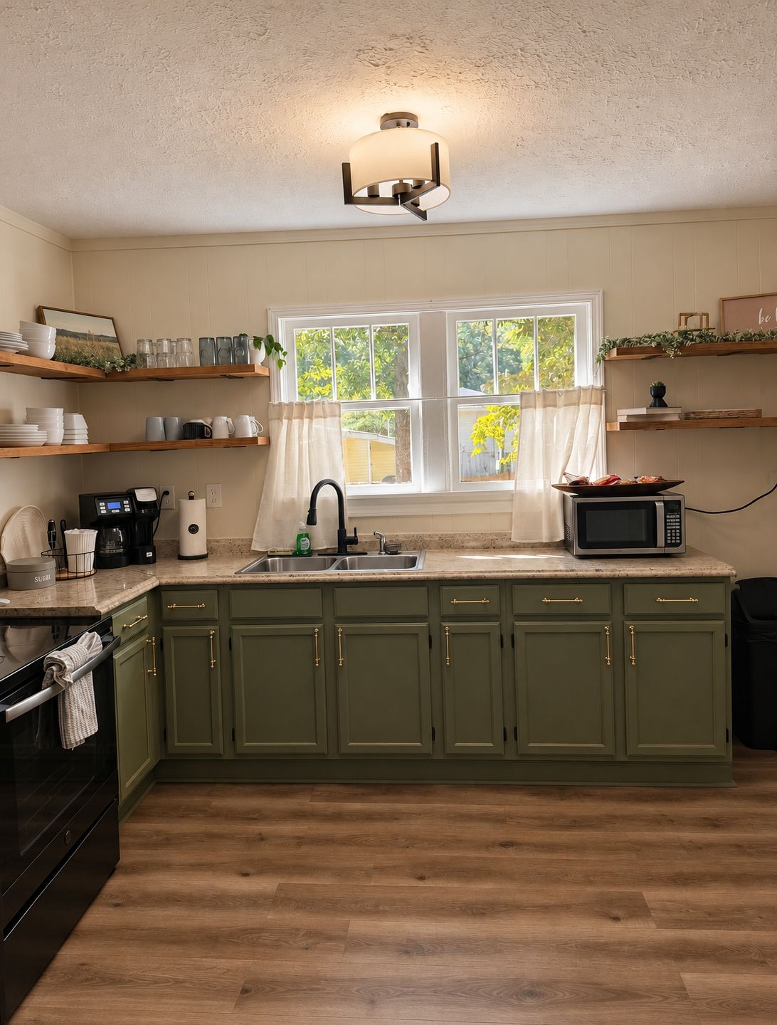 A kitchen with green cabinets, a microwave, a coffee maker, and a window with curtains.
