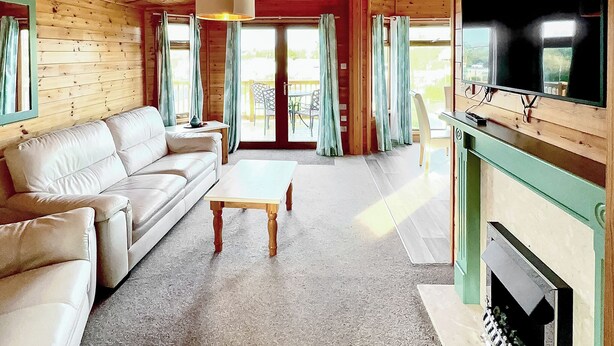 A wooden cabin interior with a sofa, a coffee table, a fireplace, and a TV mounted on the wall. - 3 bedroom accommodation in Hayle (Hayle)