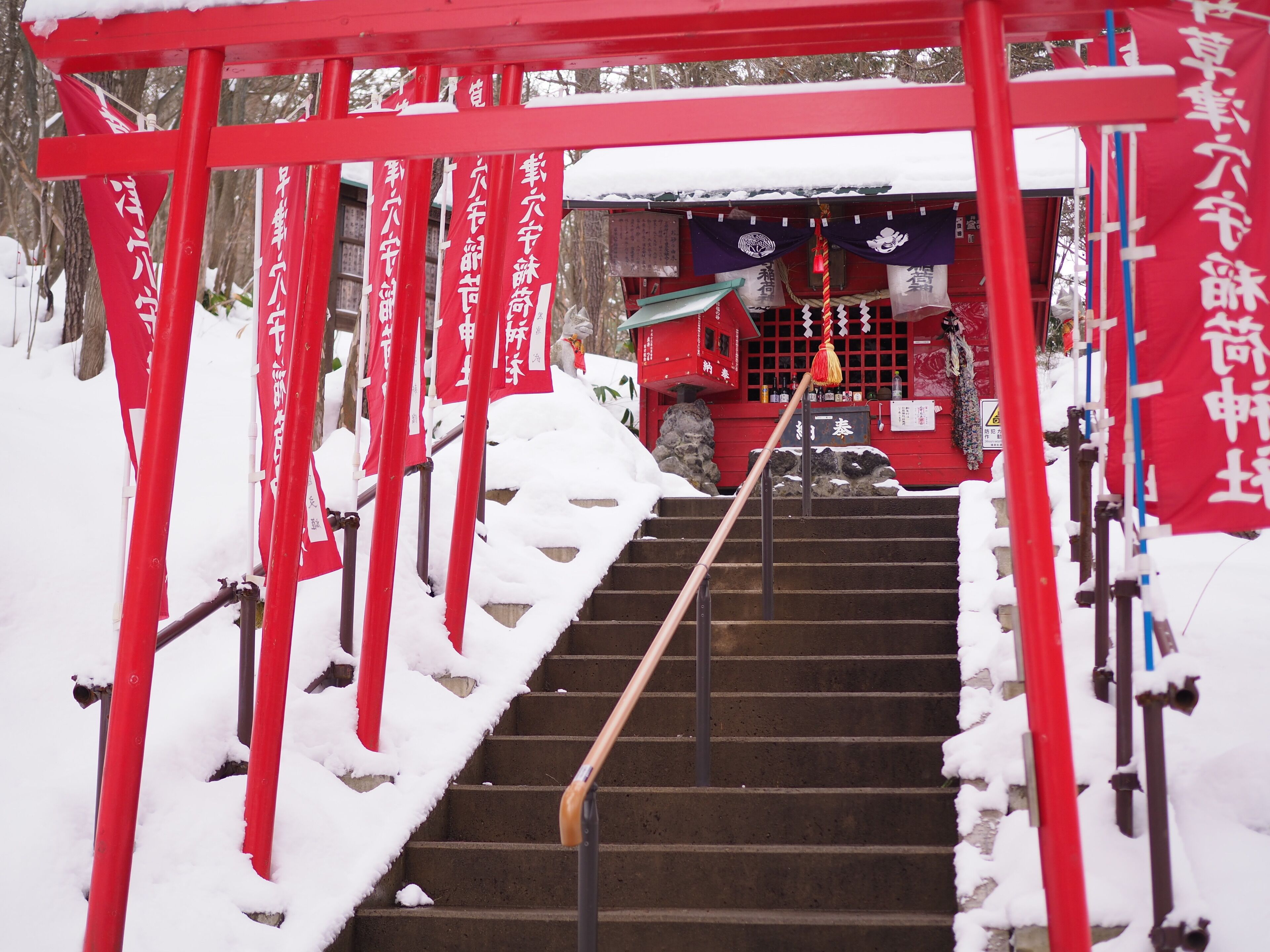 Una escalera conduce a un edificio rojo con escalones cubiertos de nieve y pilares rojos.