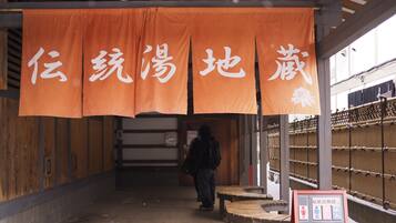 Une entrée abritée, ornée de banderoles orange, de bancs en bois et d’un panneau affichant des symboles.