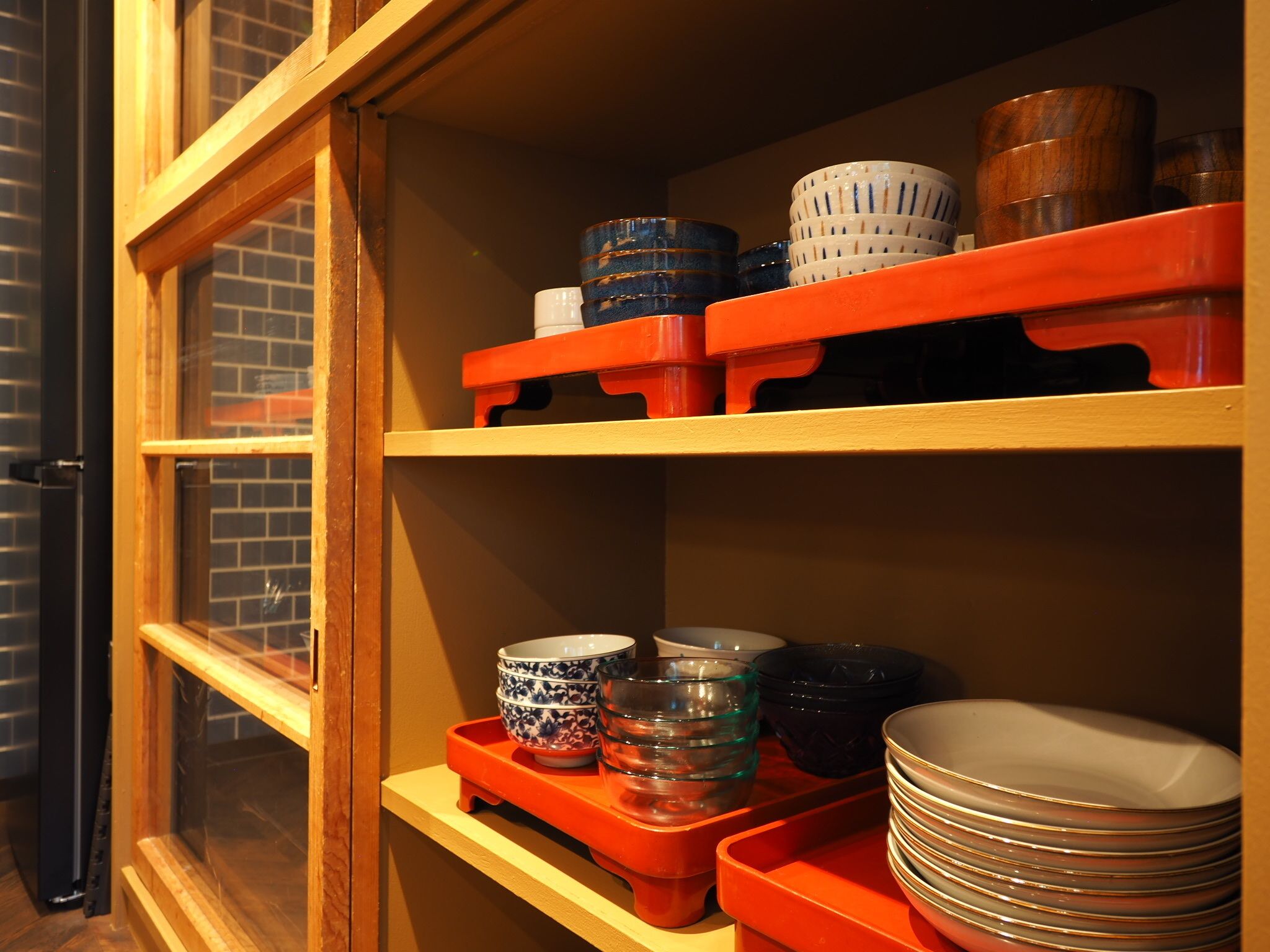 A kitchen with wooden shelves holding various bowls, plates, and a glass container.