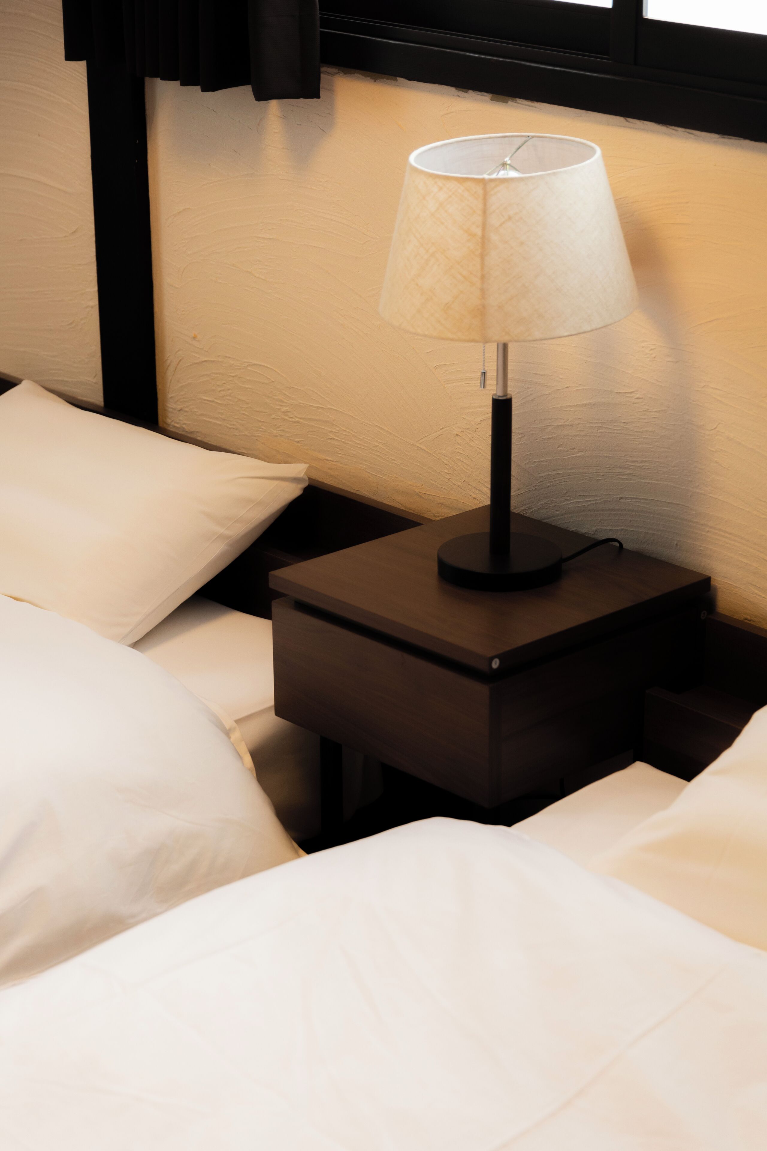 A neatly made bed with white linens and a small bedside table with a lamp.