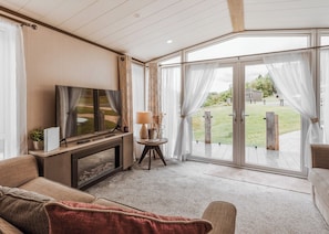 A modern living room with a flat-screen TV, a sofa, a coffee table, and a view through large glass doors to an outdoor area.