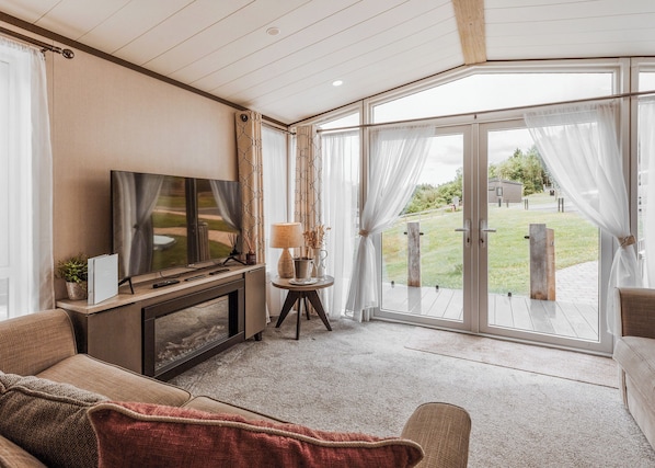 Una sala de estar moderna con televisor de pantalla plana, un sofá, una mesa de centro y vistas a un espacio exterior a través de grandes puertas de vidrio.